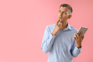 Thoughtful young man with tablet computer on pink background