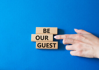 Be our guest symbol. Concept word Be our guest on wooden blocks. Businessman hand. Beautiful blue background. Business and Be our guest concept. Copy space