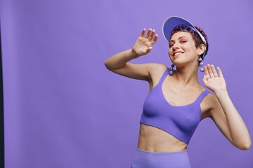 Sports fashion woman dancing posing smiling with teeth in a purple sports suit for yoga on a slender body and a transparent cap on her head on a purple background monochrome