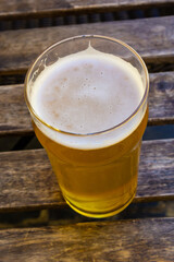 Cooled glass of beer on the wooden table. Blurred summer street cafe outside at the background.