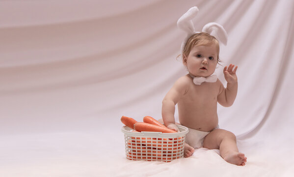 Cute baby girl with white bunny ears and basket of carrots
