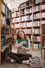Teen girl among a pile of books. A young girl reads a book with shelves in the background. She is surrounded by stacks of books. Book day.