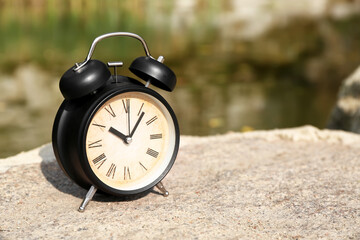 Vintage alarm clock on stone in park, closeup