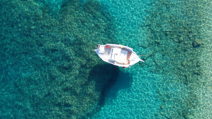 Aerial drone top down photo of beautiful wooden traditional fishing boat anchored in crystal clear emerald sea near main old port of Mykonos island, Cyclades, Greece