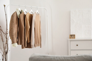Rack with stylish warm clothes near light wall in room