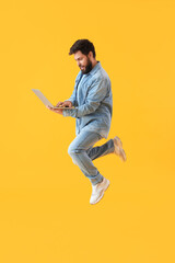Fototapeta na wymiar Handsome bearded man with laptop jumping on yellow background