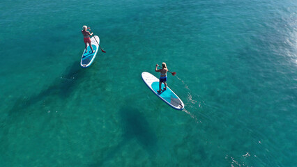 Aerial drone photo of two women practising Stand Up Paddle board or SUP surf in tropical exotic island bay with emerald crystal clear sea