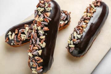 Board with tasty chocolate eclairs on light background, closeup