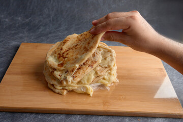 Hand picking a pupusa from a stack of pupusas on a wooden board and dark marble background