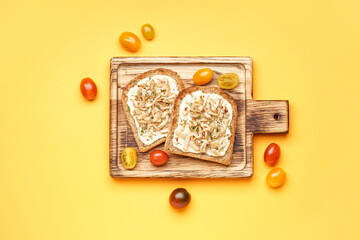 Wooden board of tasty toasts with cream cheese, mushrooms and tomatoes on yellow background