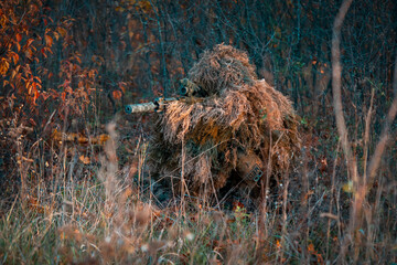 Man in a ghillie suit and with a weapon rifle outdoor.