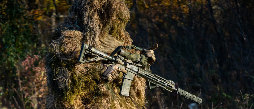 Man in a ghillie suit and with a weapon rifle outdoor.