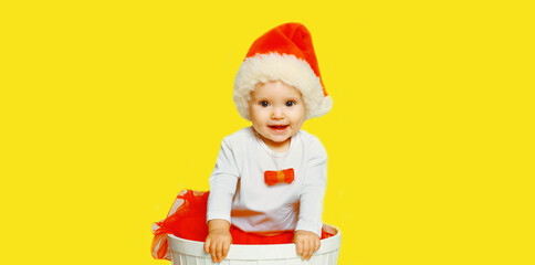 Portrait of happy smiling little child in christmas santa red hat playing with toys on yellow background