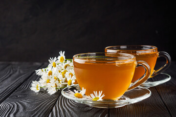 aromatic hot chamomile tea on a black rustic wooden background