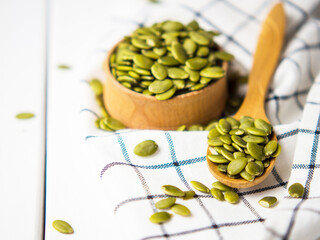 Full bowl and spoon of pumpkin seeds on a white wooden table.