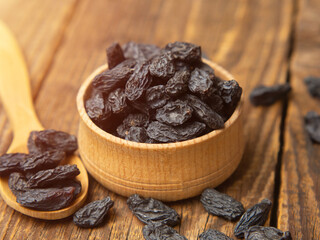 Black raisins in a wooden bowl on a textured old wood background. copy space.