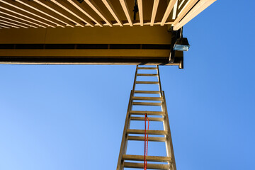 View from under an aluminum extension ladder, looking up towards roofline and blue sky
