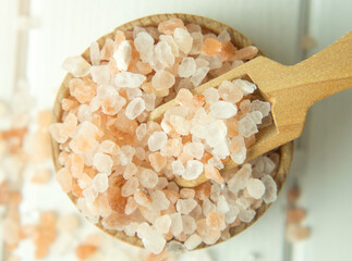 pink sea salt, heap of sea salt in a wooden bowl and scoop on a light wooden background close-up