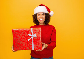 Happy woman holds in hands christmas gifts. Beautiful African American woman in santa claus hat on orange background, Looking at the camera and smiles. Xmas concept