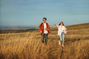 A couple is running on a big golden meadow, wearing sunglasses, smiling and enjoying the sunny autumn day.