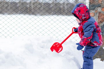 Little boy playing with a red shovel in the snow. Winter activity