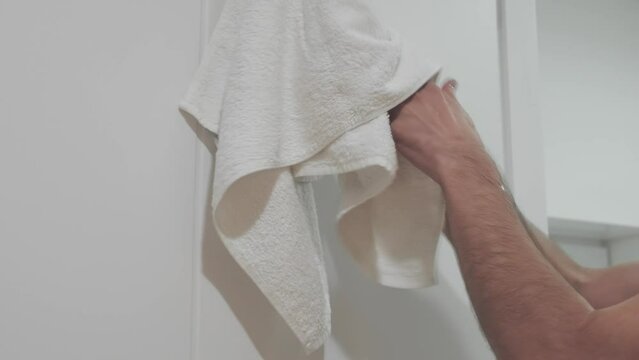 Person using towel for wiping hands dry after washing in bathroom at home. Hygiene and hand healthcare.