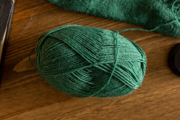 Knitting process, green woolen clew on wooden table