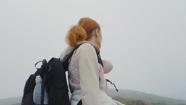 Woman traveler reaching rhododendron field having foggy backround spinning around and smiling on the top part of the mountain. Nature concept.