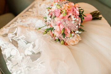 Pink wedding bouquet lies in the room on the wedding dress