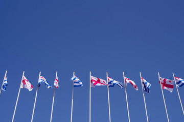 Flags of Georgia and Adjara waving in the wind against a blue sky, low angle view