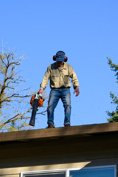 Senior Man With Gas Powered Leaf Blower Cleaning Roof Gutters On An Apartment Building, Fall Maintenance
