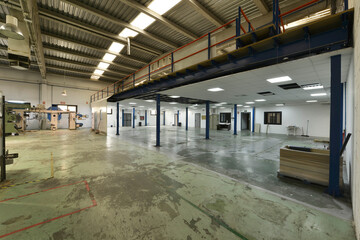 An industrial building machinery warehouse without work, several rooms and with polished concrete floors with peeling green paint and ceilings with skylights and concrete beams