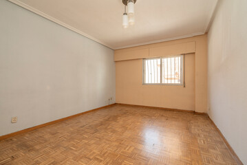 Empty room with oak parquet floor, barred window and ceiling lamp