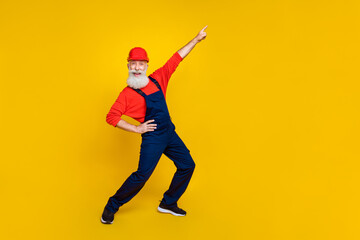 Full size photo of funky carefree builder long beard red headgear directing empty space hand on waist isolated on yellow color background