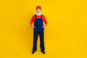 Photo of confident serious age man workwear overall red hard hat arms pockets empty space isolated yellow color background