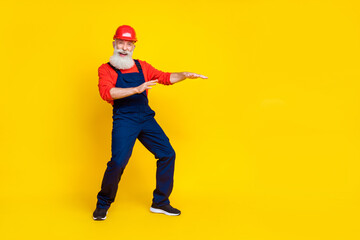 Photo of cool funny senior guy dressed uniform overall red hardhat having fun empty space isolated yellow color background