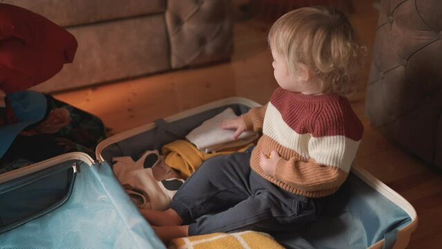 Asian mother and toddler son preparing for travel adventure, packing clothes into suitcase in cozy room, getting ready for road trip. Love and relationship concept. Mom and a kid pack luggage together