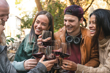 Happy group of people toasting red wine at bar outdoors-Smiling friends having fun drinking  wine together at open air  restaurant-Multicultural life style dining  concept-Focus on glass and guys