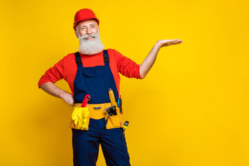 Photo of cheerful positive old guy dressed uniform overall red hardhat holding arm empty space...