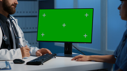 Medical staff looking at computer with green screen diplay while working late at night in hospital office. Practitioner and assistant discussing health care expertise during ckeckup visit appointment