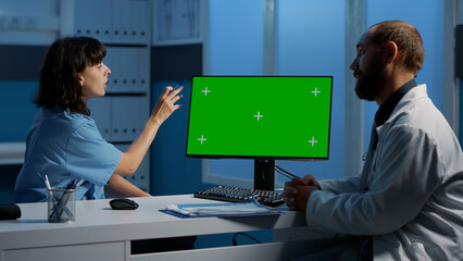 Assistant and doctor discussing patient expertise analyzing illness diagnosis report on computer with green screen template. Medical staff working late at night in hospital office, medicine service