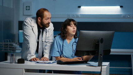 Practitioner and nurse checking medical report on computer analyzing patient disease expertise while working over hours at health care treatment in hospital office. Medicine service and concept