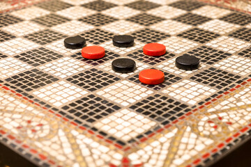 A black and white mosaic checkers table with a decorative border and red and black game pieces.