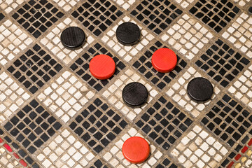 Red and black checkers on a black and white checker board made with mosaic pieces of stone.