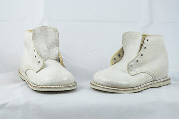 A pair of old white leather baby shoes on a white blanket background.