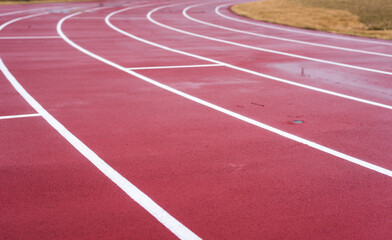 White lines mark the lanes on a wet worn red running track.