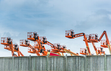 Orange colored industrial lifts peer over a wood fence.