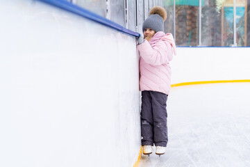 A little girl is skating on an ice rink, holding on to a support, a child is learning to skate, winter entertainment for children