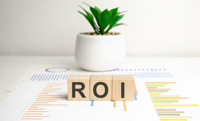 Three wooden cubes with the letters ROI on the bright surface of a grey table.