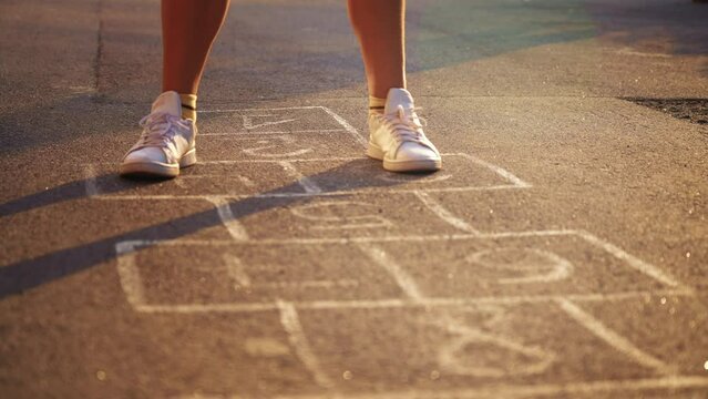 Close up legs child playing and jumping on painted on asphalt hopscotch on playground outdoors. Popular street game. Classics with numbers. Happy sport lifestyle. Summer leisure activity for people.
